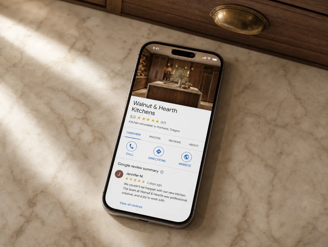 A phone on a marble counter showing a kitchen company Google Business Profile with a 5-star review and showroom photo